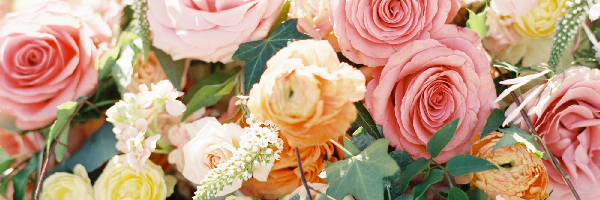 Pink, orange, and white roses interspersed with green foliage create a lush, colorful floral arrangement in natural light.